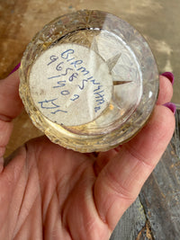 Clear glass container with star-shaped object and handwritten text held by a hand on a wooden surface.