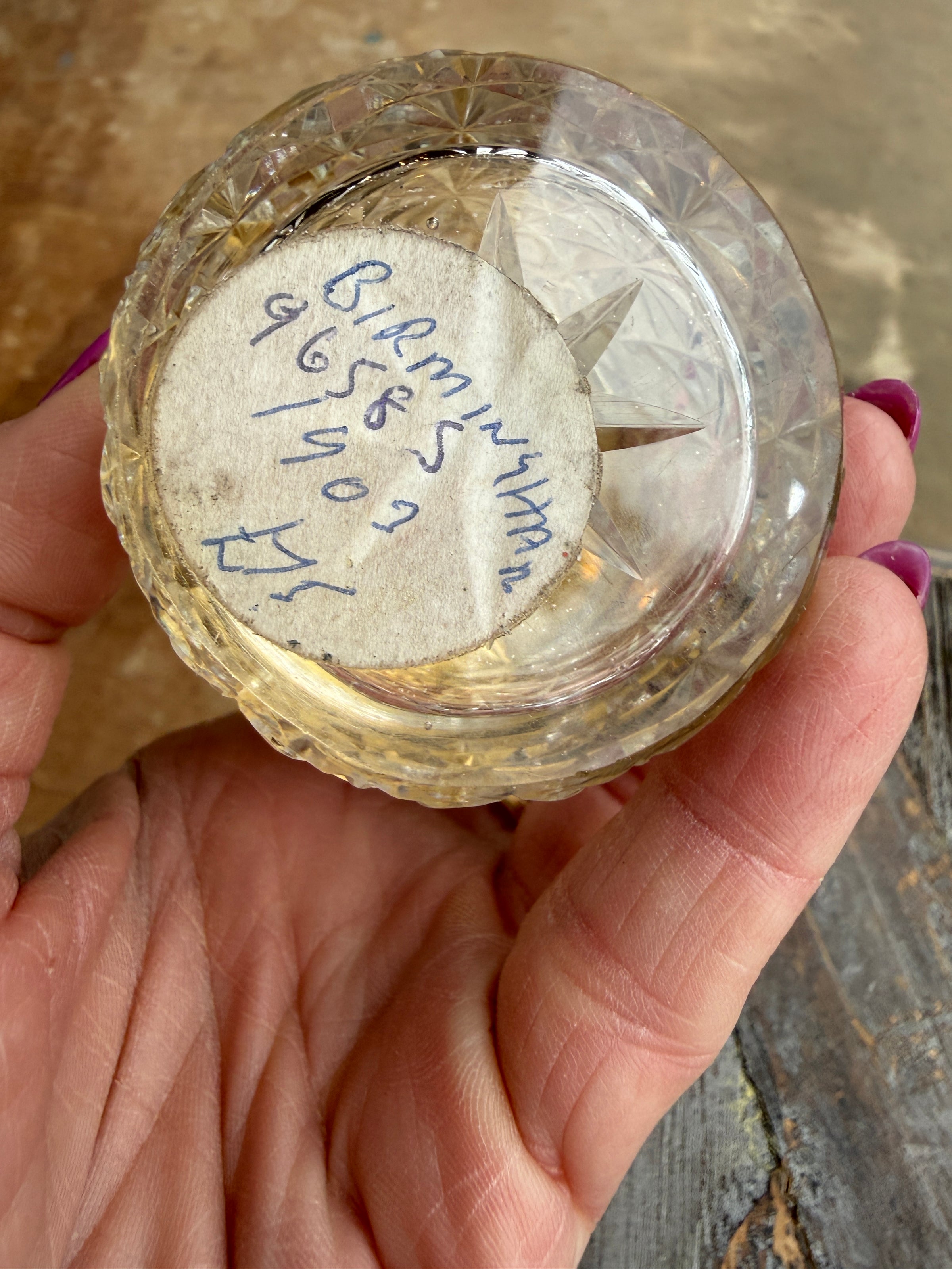 Clear glass container with star-shaped object and handwritten text held by a hand on a wooden surface.
