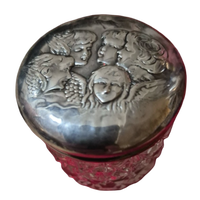 Decorative container with silver lid featuring embossed faces and red base on a white background