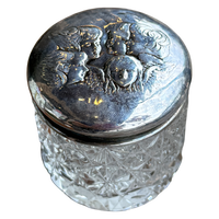 Decorative glass jar with silver lid featuring engraved faces on a white background