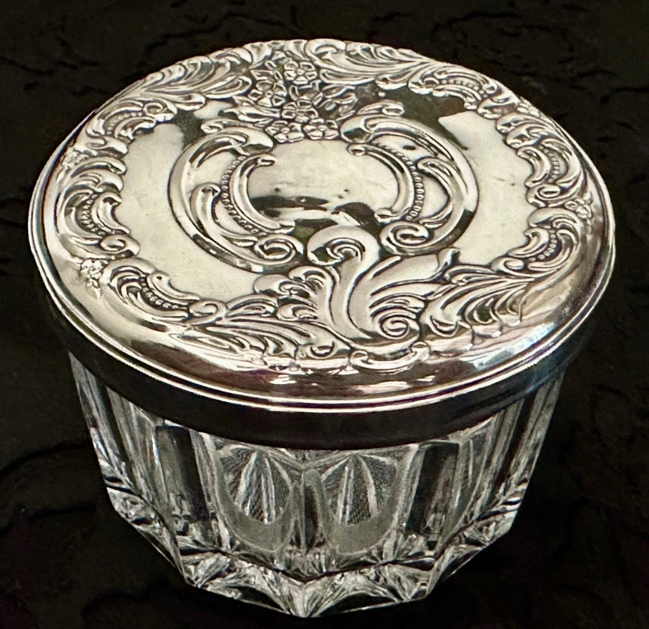 Decorative glass jar with silver lid on a dark background