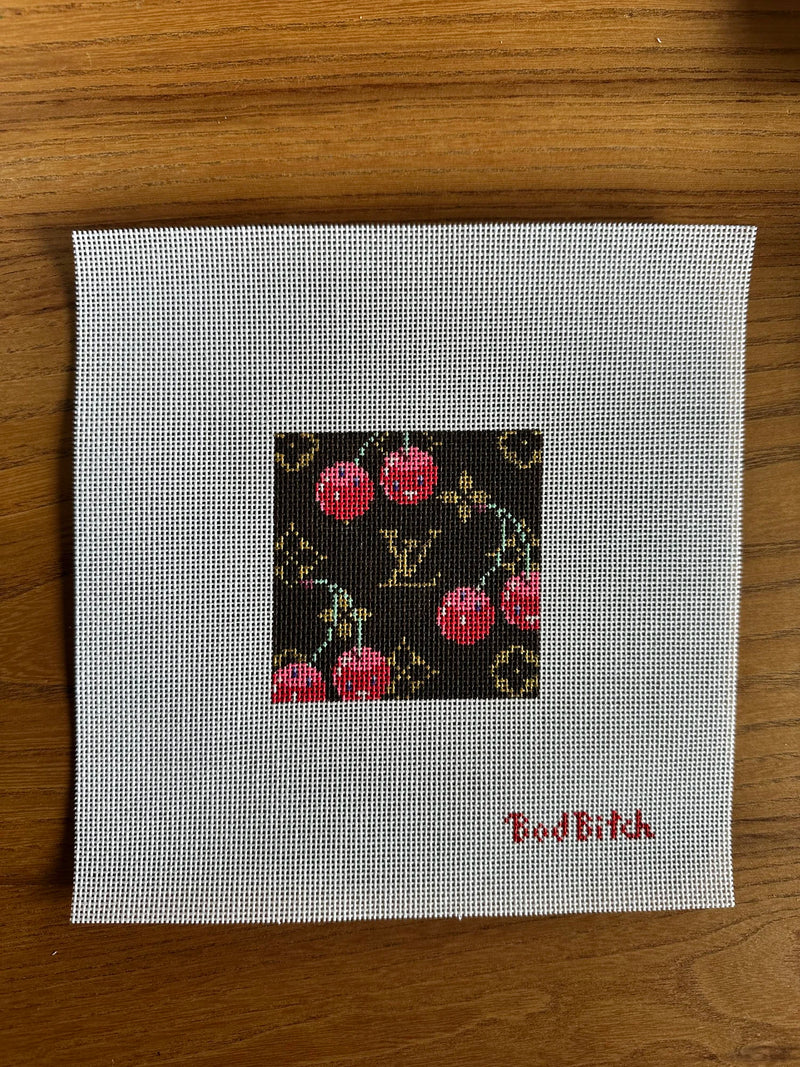 Cross-stitched design on fabric with 'Bad Bitch' text, placed on a wooden surface.