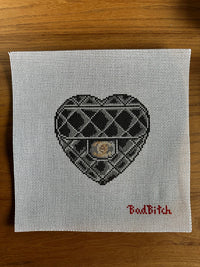 Cross-stitched heart design on fabric with 'Bad Bitch' text on a wooden surface