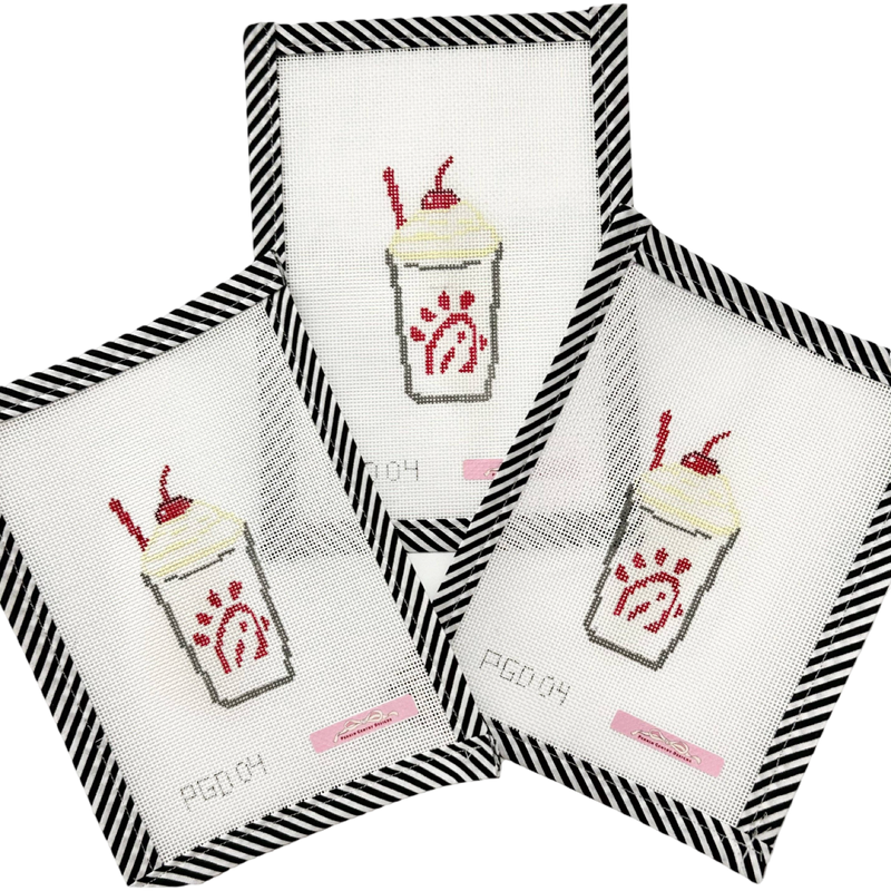 Four cross-stitched designs of a milkshake with red straw on white fabric, framed by black and white striped borders.