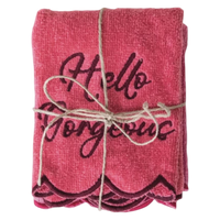 Folded pink towel with 'Hello Gorgeous' text tied with twine on a white background