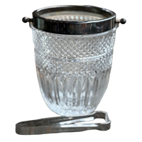 Clear glass ice bucket with black lid and silver tongs on a white background