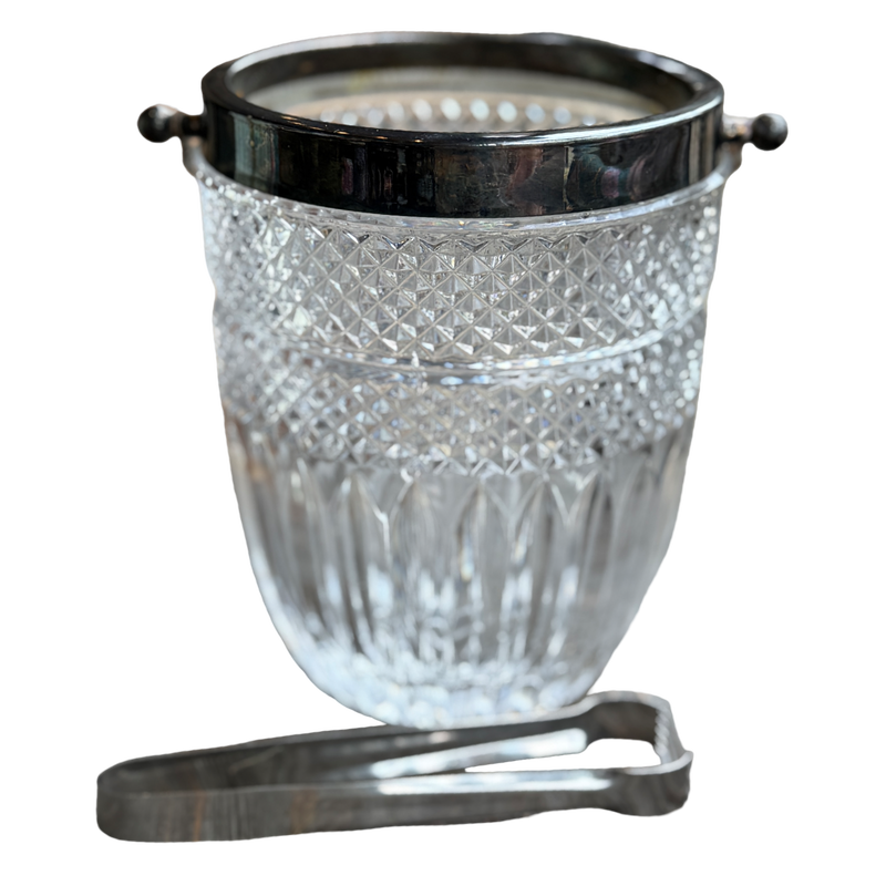 Clear glass ice bucket with black lid and silver tongs on a white background