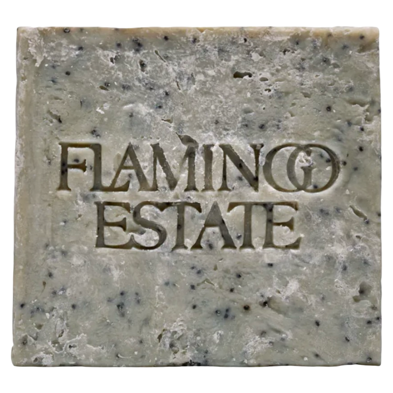 A single rectangular bar of handmade soap with a rustic, textured surface speckled with dark flecks. The brand name 'FLAMINGO ESTATE' is embossed in the center of the soap.