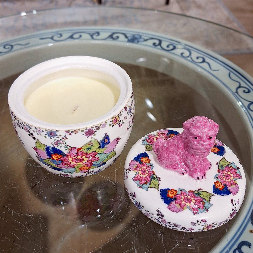 Decorative container with a pink dog figurine on a floral lid, placed on a glass surface.