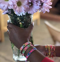 Hand holding a vase of pink flowers with colorful bracelets on a blurred background