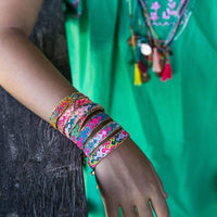 Colorful bracelets on a wrist with a green garment in the background