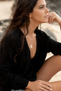 Woman wearing a black top and gold jewelry sitting outdoors.