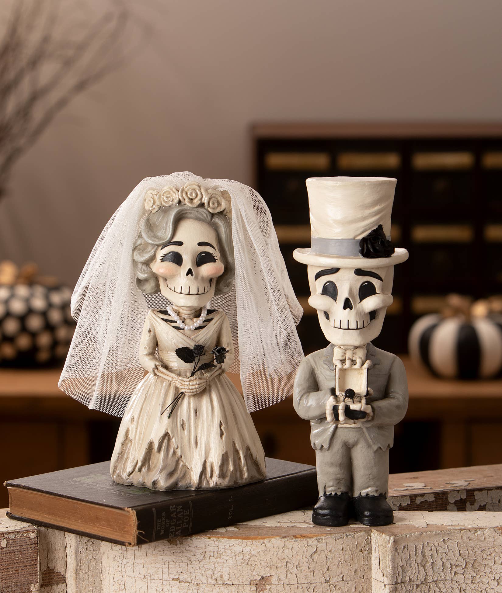 Skeleton bride and groom figurines on a rustic surface with pumpkins in the background.