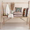 Bamboo shelf with decorative pillows, a vase, and a blanket against a neutral wall.