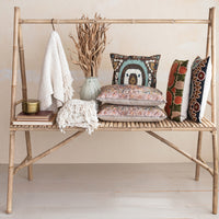Bamboo shelf with decorative pillows, a vase, and a blanket against a neutral wall.