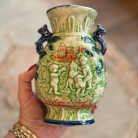 Hand holding a decorative ceramic vase with intricate designs.