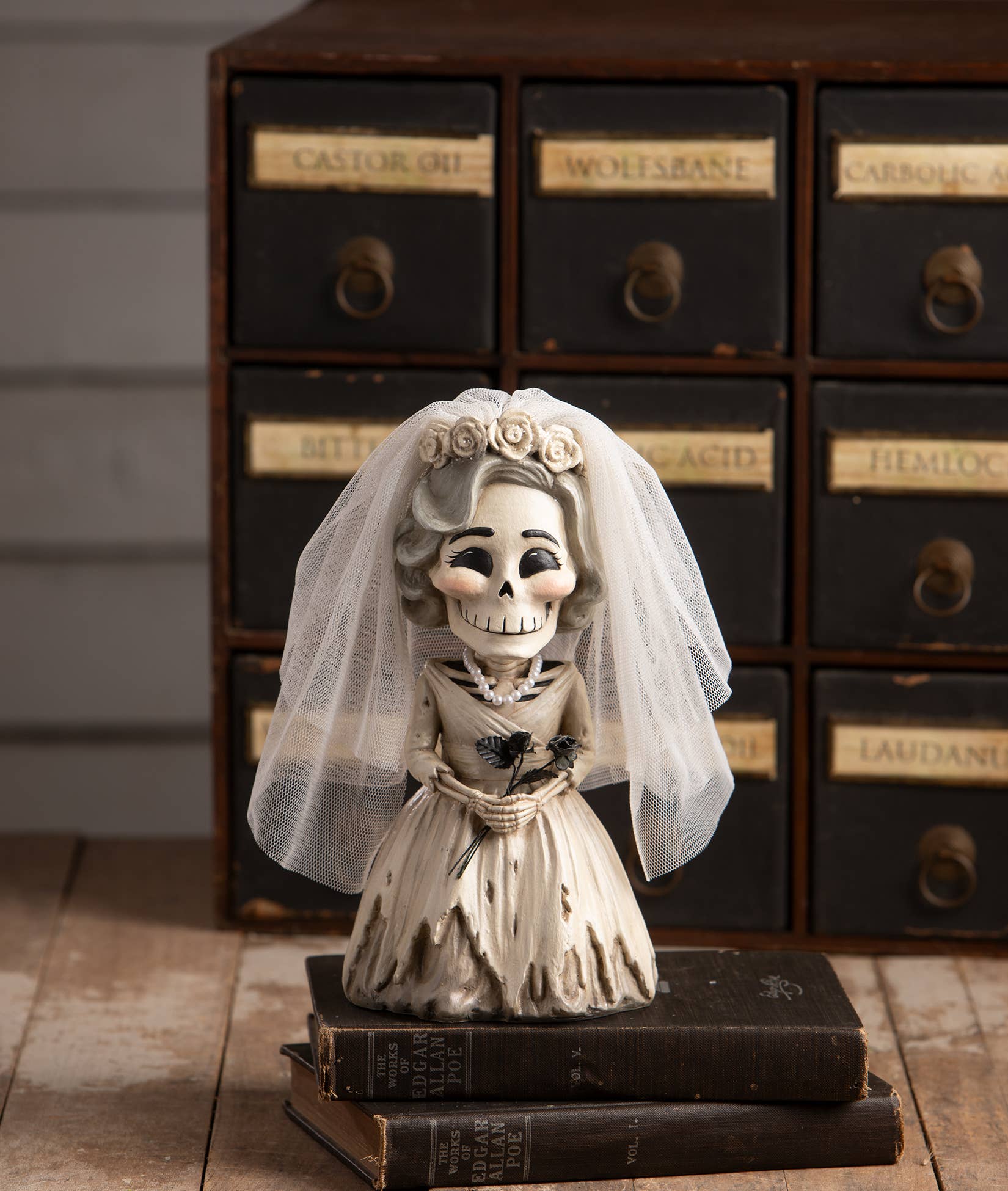 Skeleton bride figurine in a wedding dress with a veil on a wooden surface with vintage drawers in the background.