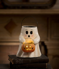 A ghost-shaped ceramic Halloween candle holder with a black wire handle, holding a glowing jack-o'-lantern. The ghost has a white body with black facial features and subtle pink blush marks.