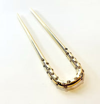 A gold U-shaped hair pin or hair stick decorated with small round rhinestones along the lower curve, photographed on a clean white background.