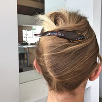 A close-up back view of a person with light brown hair styled in a messy bun, secured with a tortoiseshell hair clip, in an indoor setting.