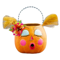 An orange pumpkin-shaped Halloween bucket basket with a handle, featuring cartoon eyes, pink cheeks, a surprised mouth, yellow feather-like hair accents, and a flower decoration on the side, isolated on a white background.