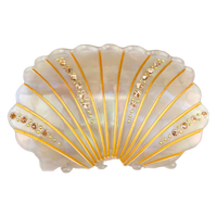 A scalloped shell-shaped dish with an iridescent white and pale pink shell-like surface, decorated with gold radial lines and rows of small rhinestones, shown on a plain white background.