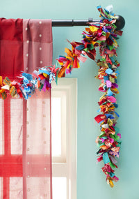 Colorful fabric garland hanging on a curtain rod against a light blue wall.
