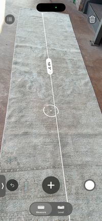 A long gray textured rug laid flat on a concrete floor, with a white measurement overlay showing its length and a circular marker highlighting a section.