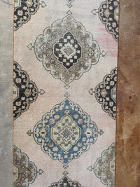 A close-up of a patterned area rug with traditional medallion motifs. The rug features a dusty pink background with blue, beige, and black ornamental medallions.