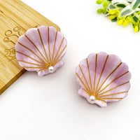 Pink shell-shaped earrings with gold accents and pearls on a white background