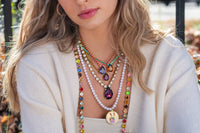 Close-up of a person wearing multiple colorful necklaces with a blurred outdoor background