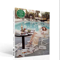 Book cover with a woman by a poolside, featuring a table with a statue and books.