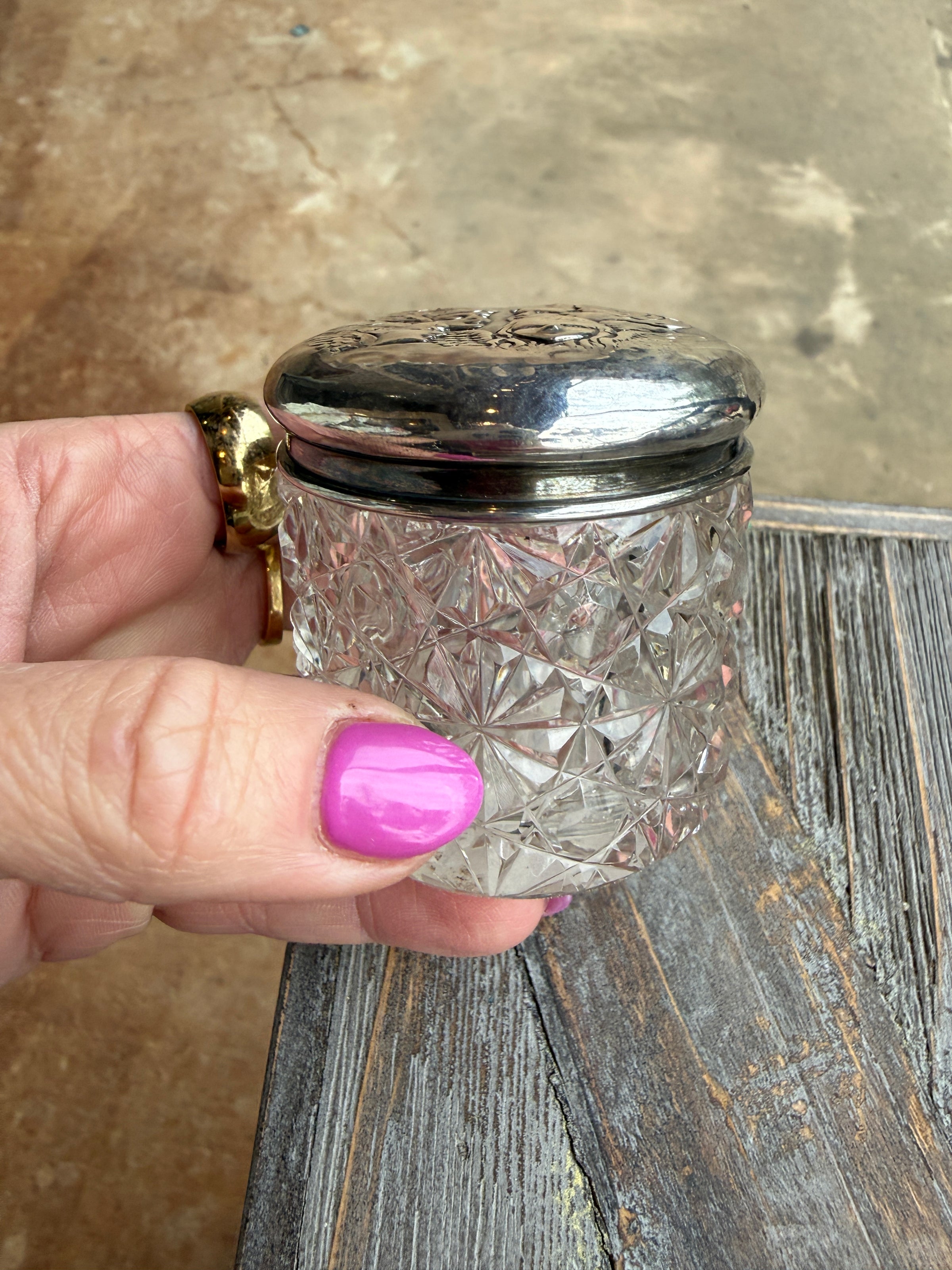 Hand holding a decorative crystal container with silver lid against a wooden surface.
