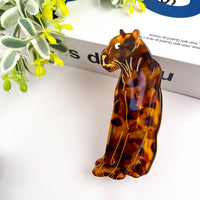 Tortoiseshell cat-shaped hair clip on a white surface with green leaves in the background