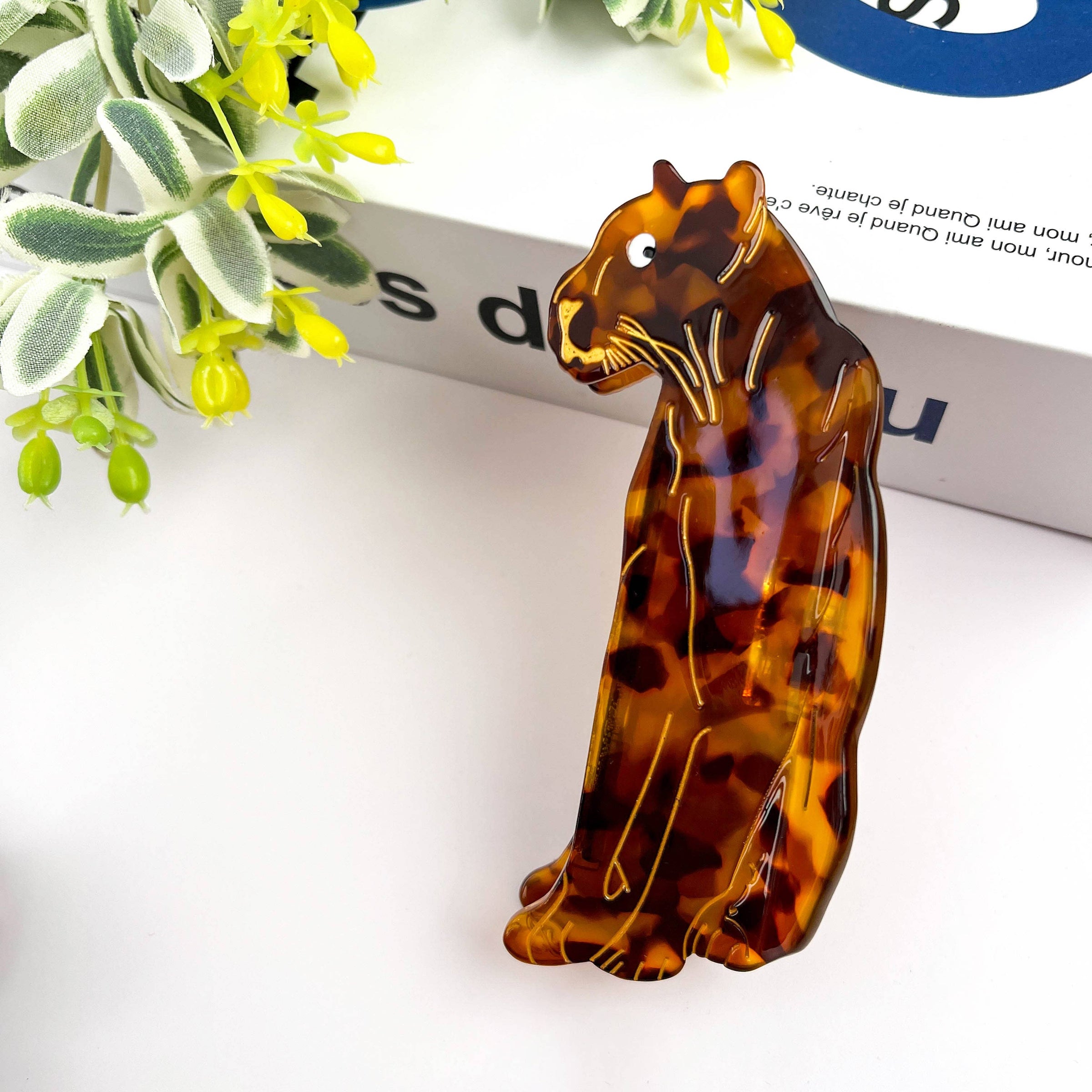Tortoiseshell cat-shaped hair clip on a white surface with green leaves in the background