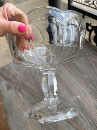 Clear glass wine glass held by a hand with pink nail polish on a wooden surface.