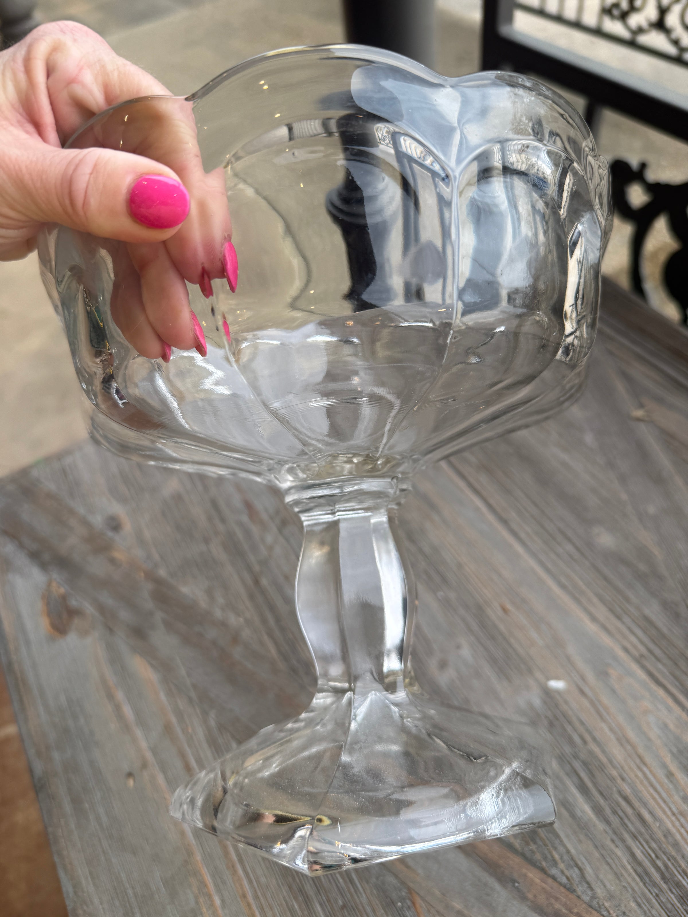 Clear glass wine glass held by a hand with pink nail polish on a wooden surface.