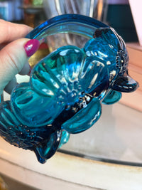 Blue glass object resembling a fish held by a hand with a blurred background