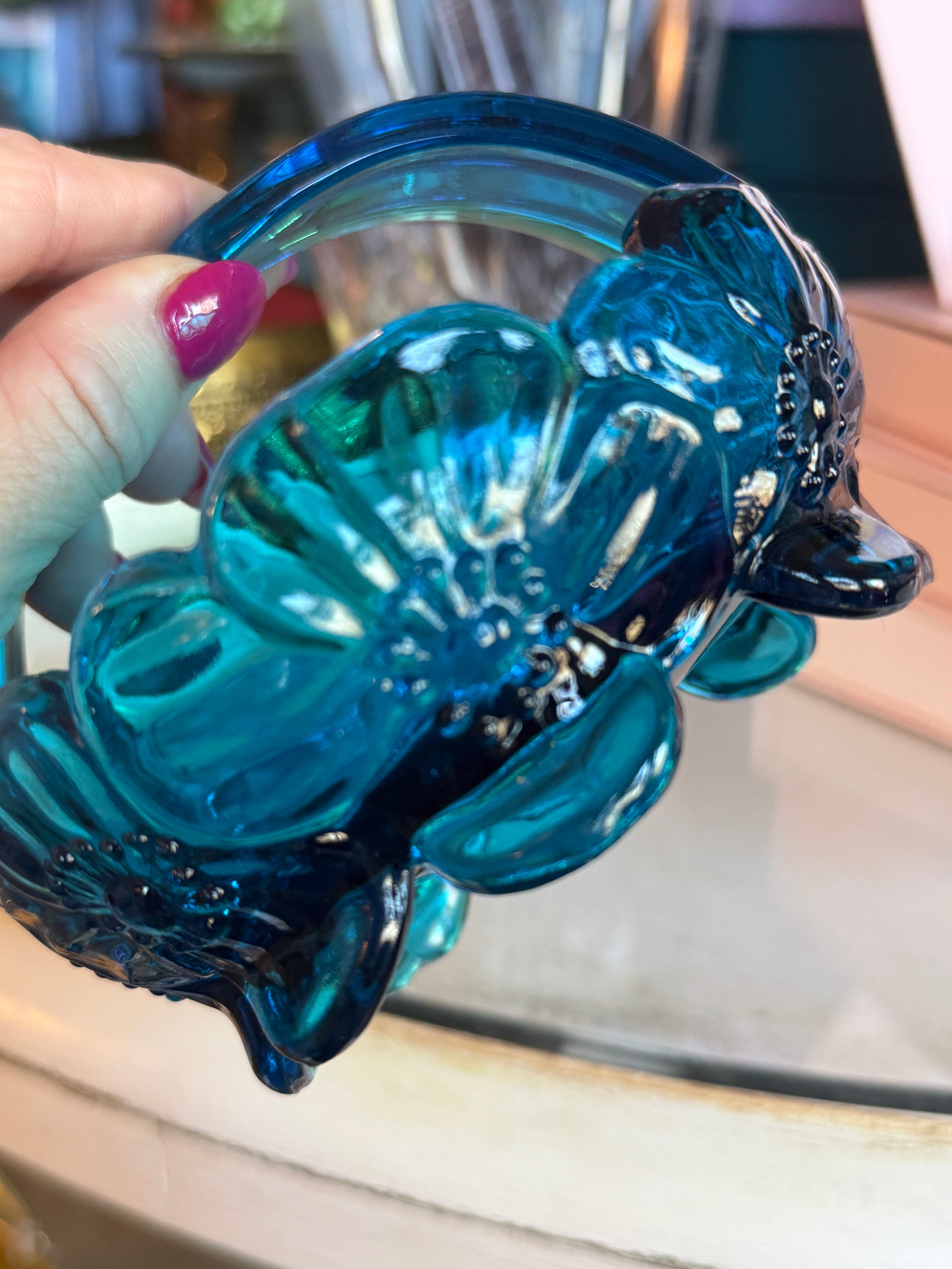 Blue glass object resembling a fish held by a hand with a blurred background