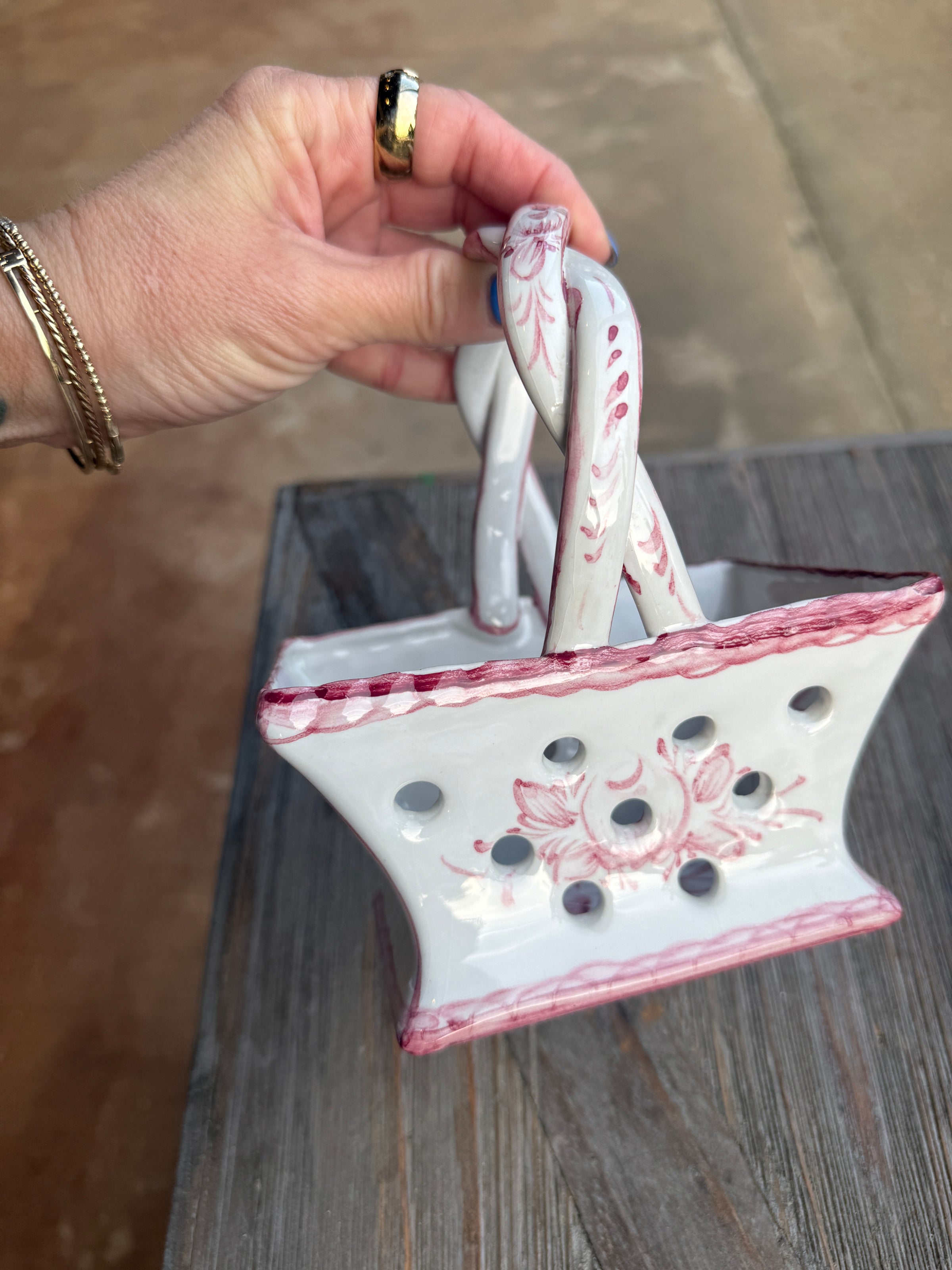 Hand holding a decorative white and pink ceramic pot with floral patterns on a wooden surface.