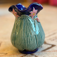 Small ceramic vase with a textured green body and blue top on a patterned surface