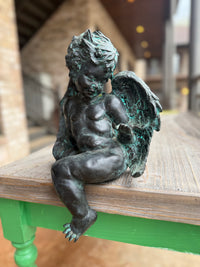 Bronze statue of a winged figure on a wooden bench with a blurred background