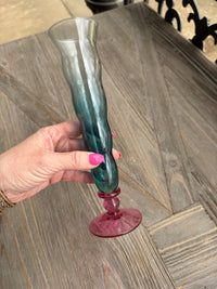 Glass object with a pink base held by a hand on a wooden surface