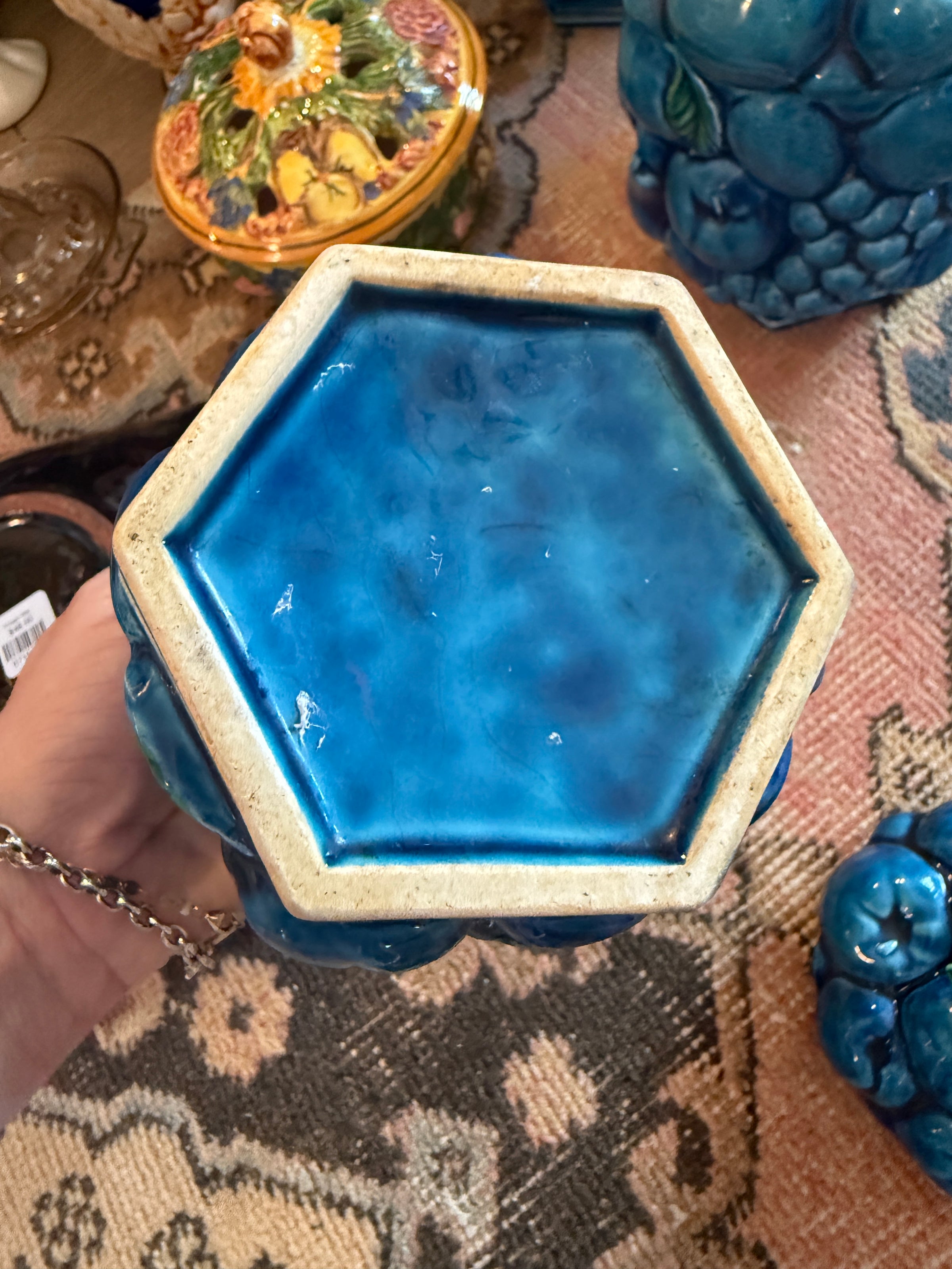 Hexagonal blue ceramic object held by a hand on a patterned surface