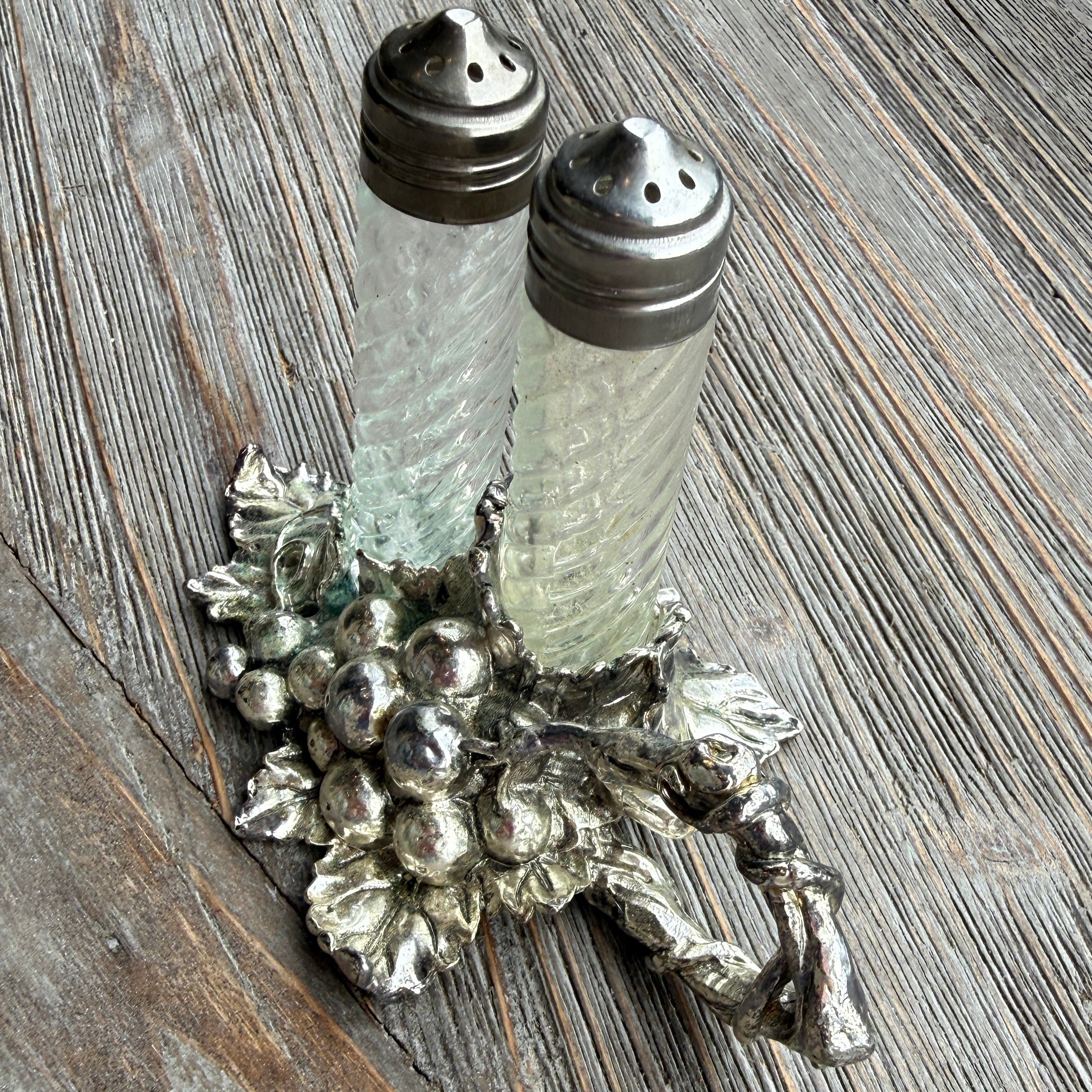 Decorative silver salt shaker holder with glass salt and pepper shakers on a wooden surface