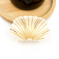 White acetate shell-shaped claw clip decorated with sparkling rhinestones.