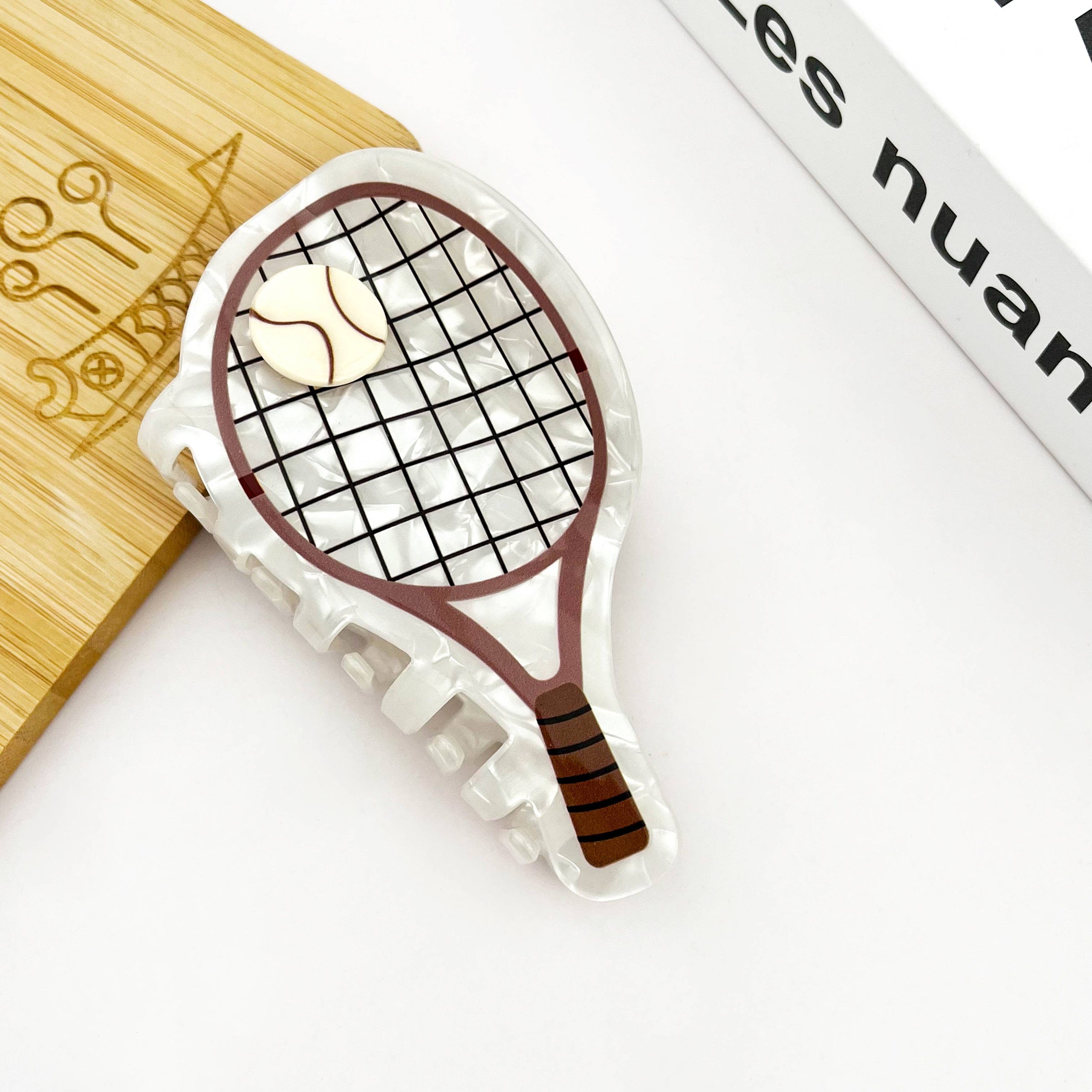 White acetate tennis racket-shaped claw clip designed as a sporty statement hair accessory.