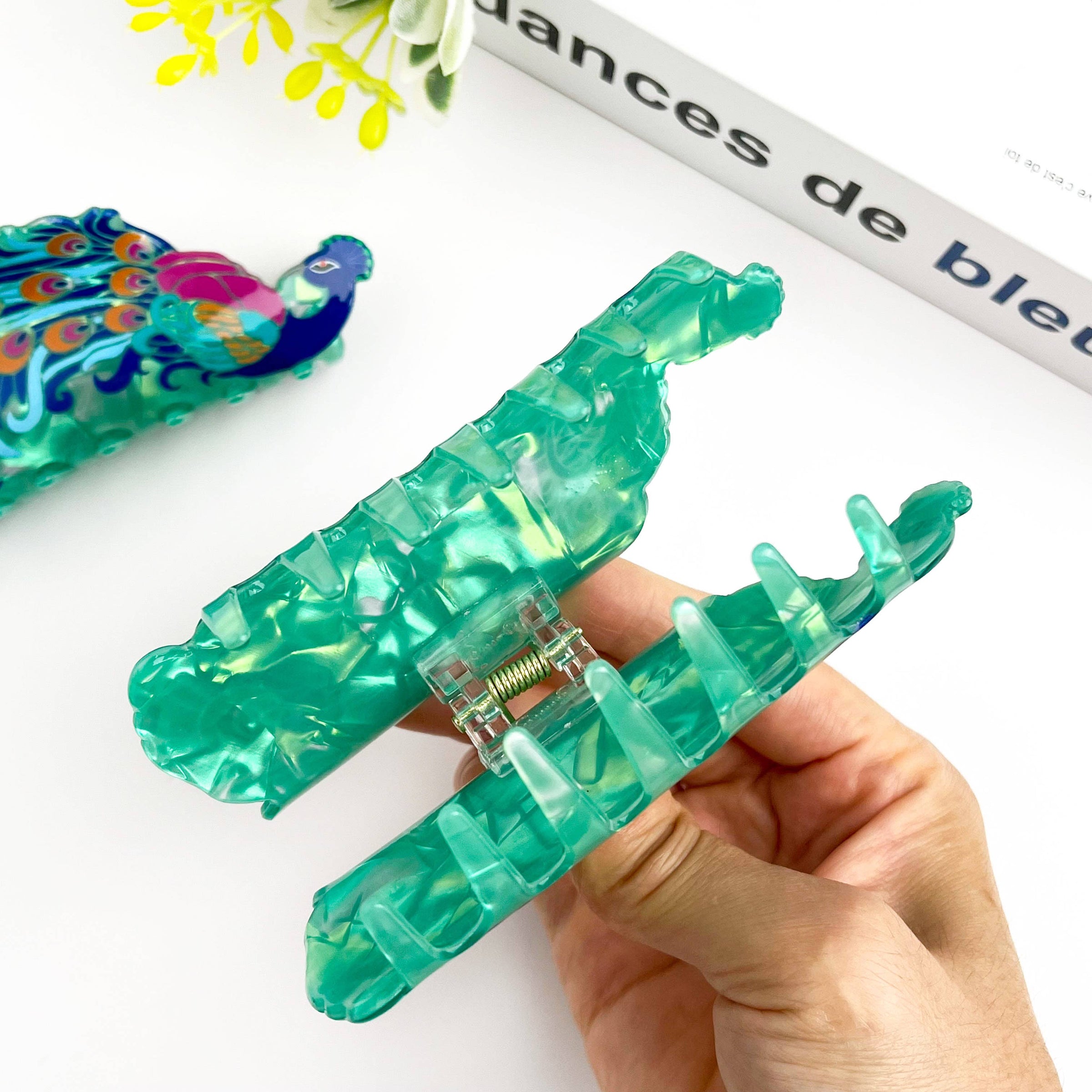 Green plastic tool held by a hand with a blurred magazine in the background