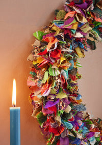 Colorful fabric wreath with a lit candle on a plain background