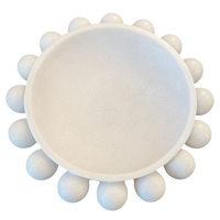 A white ceramic or stone round dish with a raised rim and multiple small rounded protrusions around the edge, shown on a plain white background.
